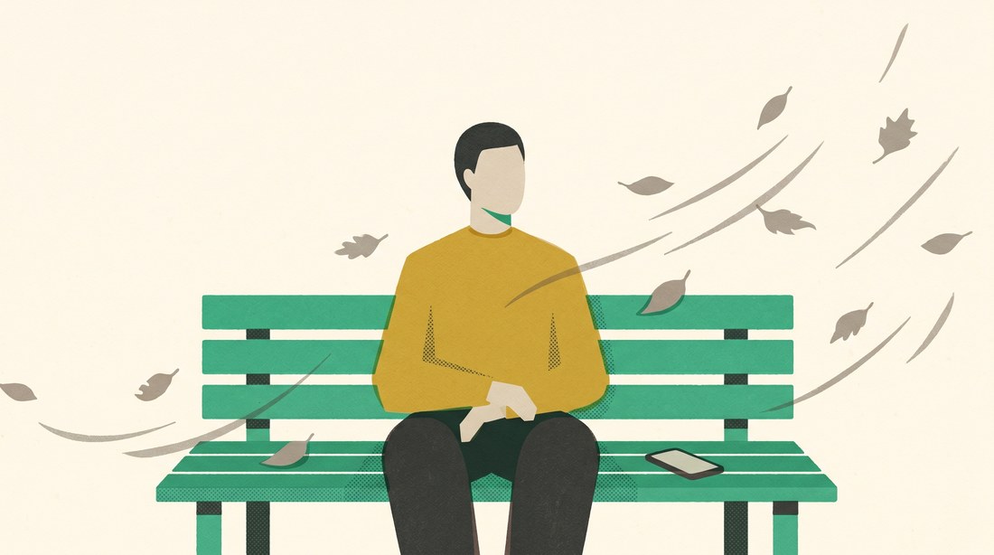 A person on a park bench, leaves blowing in the wind, phone face-down on the seat beside them — steady amid noise